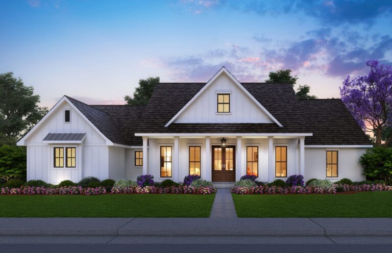 A front view of a modern farmhouse-style home with a warm and inviting design. The exterior features white board and batten siding, a dark shingled roof, and large windows that allow natural light to illuminate the interior. The entryway includes a covered front porch supported by white columns, leading to double wooden front doors. The front yard is beautifully landscaped with a lush green lawn and vibrant flower beds filled with pink and purple flowers, creating a welcoming atmosphere. Tall trees surround the home, with the sky painted in soft hues of blue and pink as the sun sets, adding to the serene and charming setting.