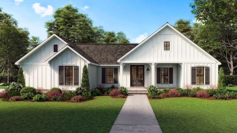 A front view of a modern farmhouse-style home with a simple yet elegant design. The exterior features white board and batten siding, a dark shingled roof, and dark shutters framing the windows. The entryway includes a covered front porch with arched details, leading to double wooden front doors. The front yard is beautifully landscaped with a lush green lawn, shrubs, and colorful flower beds. Tall trees provide a natural backdrop under a clear, bright blue sky, enhancing the home's welcoming and serene atmosphere.